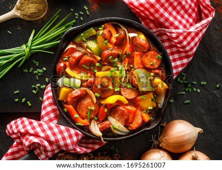 Stewed pepper and sausage with tomatoes in a cast iron skillet on a black background, top view. Traditional Hungarian stew called lecho  Stock fotó © 