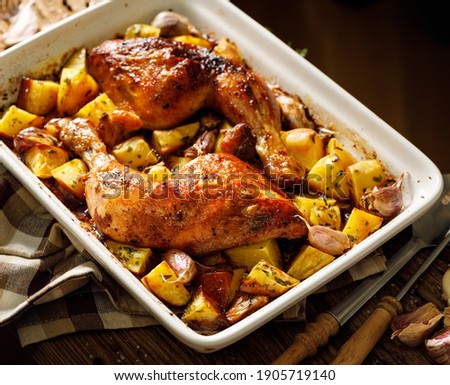 Baked chicken leg quarters  seasoned with garlic and herbs with potatoes in a baking dish on a wooden table close up view