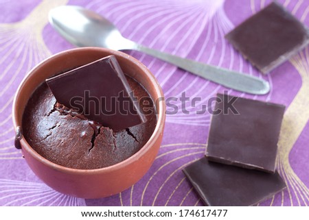 Traditional french chocolate fondant cake with melted heart in natural brown earthenware cup with a spoon. Natural blown and purple background with broken chocolate pieces.