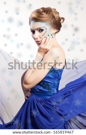 Portrait of winter cold woman with snow splash. Christmas girl. Beauty model lady. Winter makeup and hairstyle. Blue fluttering dress.