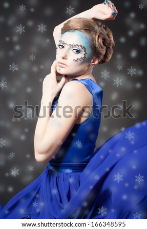 Portrait of winter cold woman with snow splash. Christmas girl. Beauty model lady. Winter makeup and hairstyle. Blue fluttering dress. Snow queen.