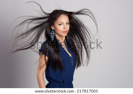 Beautiful close-up portrait of a young woman with healthy long windy hair. Blue dress and jewelry. Fashion shot.