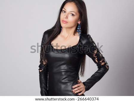 Attractive and sexy portrait of a long hair young woman in black leather dress in studio. Naked back. Fashion and glamour shot.