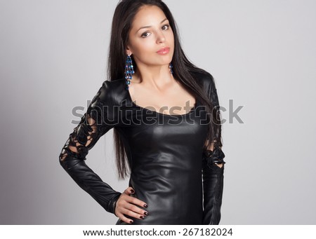 Attractive and sexy portrait of a long hair young woman in black leather dress in studio. Naked back. Fashion and glamour shot.