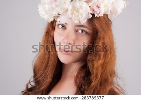 Beautiful close-up potrait of a woman with peonies wreath. Spring care concept. Natural look. Long red hair.