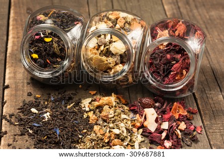 Dry tea in glass jars on wooden rustic background. Leaves of red, green and black tea. Macro photo. Rustic style and concept.
