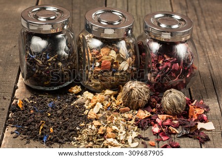 Dry tea in glass jars on wooden rustic background. Leaves of red, green and black tea. Macro photo. Rustic style and concept.