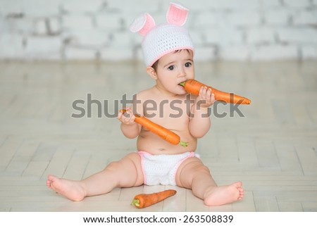 Portrait of a cute baby dressed in Easter bunny ears sitting and eating a carrot