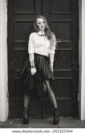 Black and white photography. Model in a black leather skirt and white blouse near the wooden door