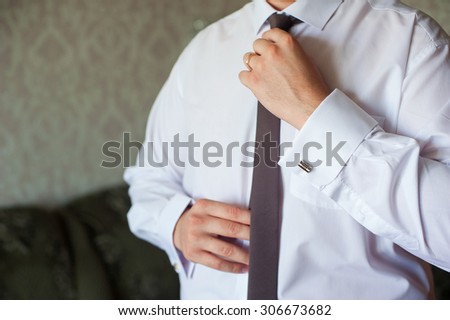 Man in a white shirt with cuff links, straightens his tie