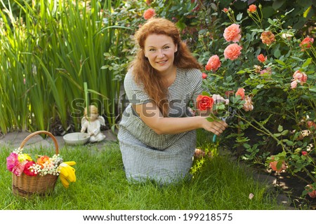 attractive adult woman cuts flowers roses in country house on nature