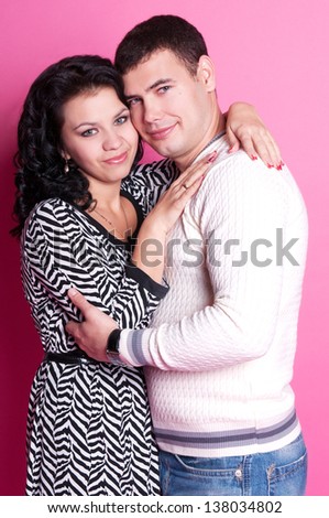 happy attractive young couple in love - romantic girlfriend and boyfriend on pink background isolated in studio