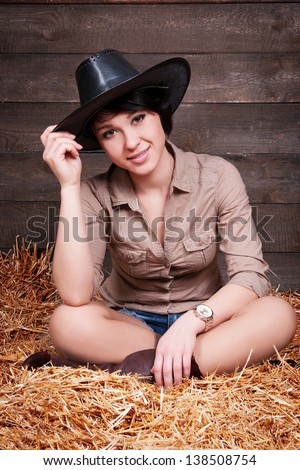 Fashion beautiful sexy cowgirl in jeans shorts and a shirt at the ranch farm. pinup and wild west western style. happy smiling slim girl on hay at farm. Fashion and pinup romantic american style.