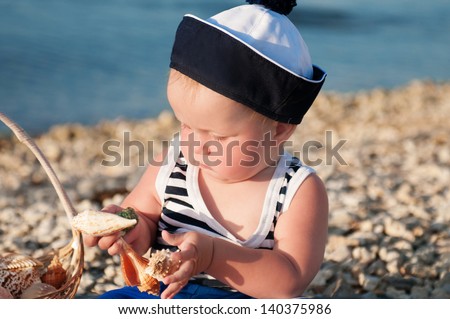 happy little child in a suit of the seaman smiling and having fun on the sea. adorable cute babe playing and resting on nature. trendy blond funny child on nature enjoying the sun in park and posing