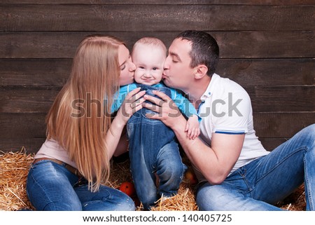 Happy family with the child - beautiful mother and father hug their son, posing on hay in studio closeup