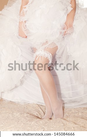 Garter on the leg of a bride, slim sexy bride in wedding luxury dress showing her silk garter. woman have a final preparation for wedding ceremony. Wedding day moments