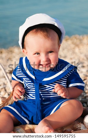 happy little child in a suit of the seaman smiling and having fun on the sea. adorable cute babe playing and resting on nature. trendy blond funny child on nature enjoying the sun in park and posing