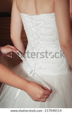 Morning bride. maid of honor helping the bride with her dress. bridesmaid tying bow on wedding dress. helping to lace up bride\'s wedding dress