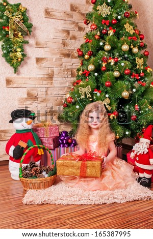 Christmas kid with New Year Tree and xmas gift. Winter concept/ Portrait of Happy Christmas girl at home. Happy New Year. Luxury house at New Year. Small girl in santa with present have a christmas.