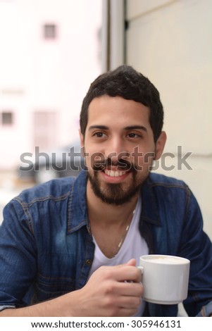 Young latin handsome man drinking coffee at an outdoor cafe.