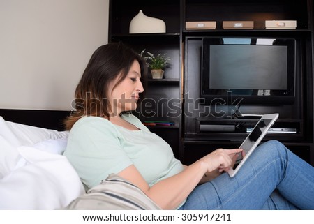 Middle age latin woman using her tablet in bed.