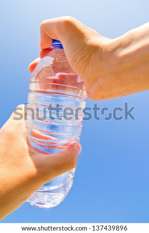 Hand opening the lid of the bottle isolated on a blue background of sky