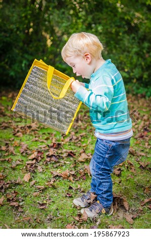Cute surprised little blond boy is looking inside a bag at park