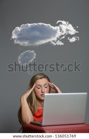 Blond woman sitting in front of her laptop with her eyes shut with dark clouds above her.