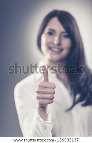 Smiling attractive woman making a thumbs up sign of praise, approval and success with selective focus to her hand and shallow depth of field