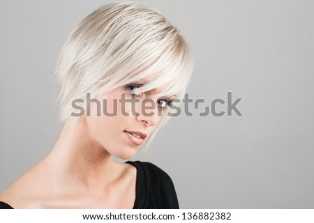 Beautiful young woman with a trendy blonde hairstyle, head and shoulders portrait on a grey studio background