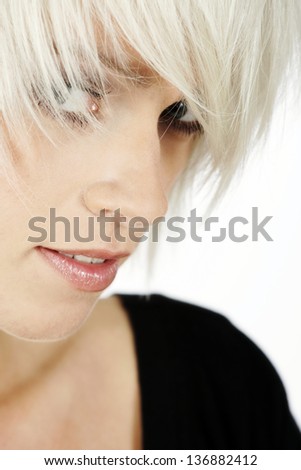 Closeup portrait of a young sexy blonde woman with a trendy hairstyle peering sideways at the viewer through her hair