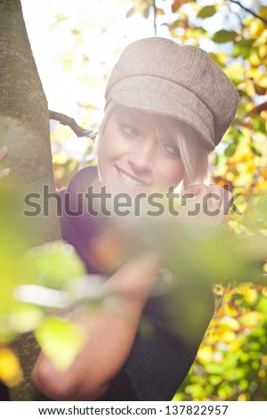 Trendy modern young blonde woman wearing a peaked cloth cap photographed through autumn foliage