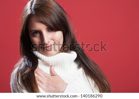 Gentle woman in a polo neck pullover looking at the camera with a serene expression, isolated studio portrait on red