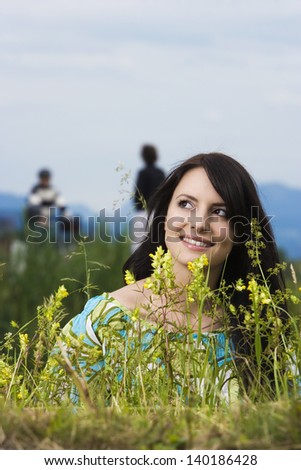 Serene young woman in nature standing behind greenery and foliage looking up into the blue sky with a faraway dreamy expression