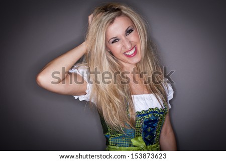 Beautiful smiling blond woman in a dirndl with her head tilted to one side and her hand to her hair giving the rather freaky appearance that she is holding her head in place with her hand