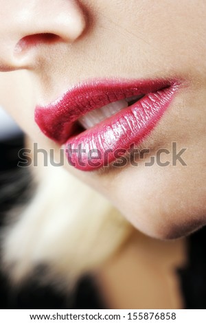 Sexy female lips of a beautiful young woman with crimson lip gloss parted to reveal the teeth in a seductive manner