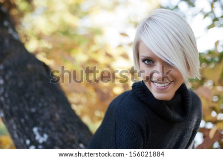 Pretty blond student in a fall garden leaning towards the camera with a beautiful friendly smile