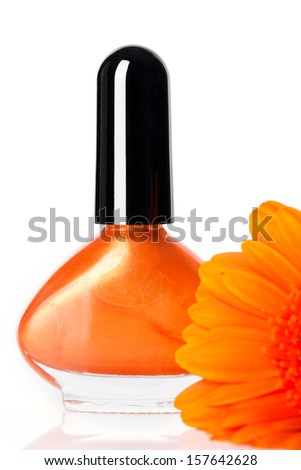 Modern trendy orange nail varnish in a stylish globular bottle with a fresh Gerbera daisy in the foreground over white