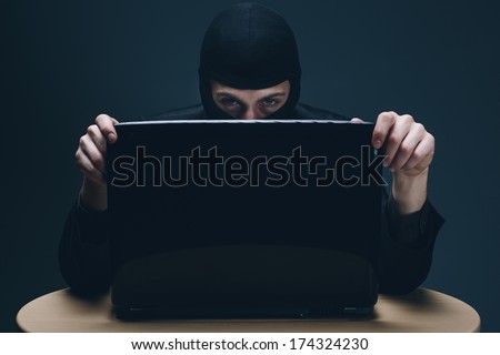 Furtive masked hacker accessing a laptop computer to steal data, plant malware or spy conceptual of cyber crime, online security and identity theft