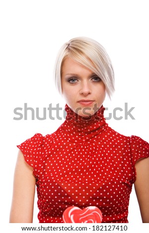 Beautiful elegant blond woman in a high necked ed top holding a heart shaped Valentine lollipop while looking directly at the camera with a serious expression, isolated on white with copy space
