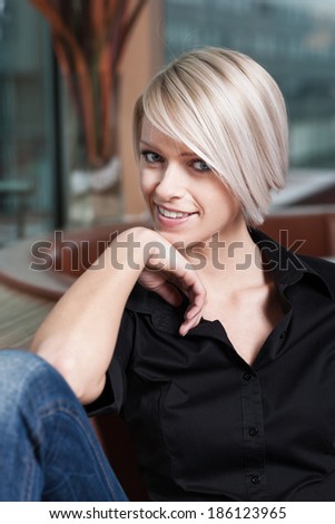 Happy relaxed young woman in a bar sitting with her hand to her chin looking at the camera with a friendly smile