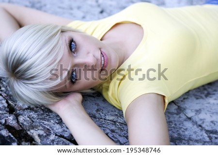 Beautiful blue-eyed blond woman lying back on a rock with her hands clasped behind her head looking up at the camera