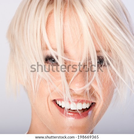 Laughing beautiful young woman with funky blond hair hanging in wisps all over her face , close up face portrait