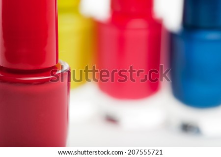 Closeup of a jar of colorful red modern nail lacquer or varnish with three colorful blue, pink and yellow bottles visible as a blur behind, with copy space