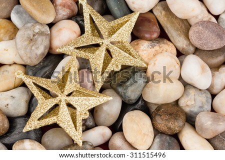 Christmas star ornaments on pebbles - Gold glitter star ornaments set on multi colored stones as Christmas background.