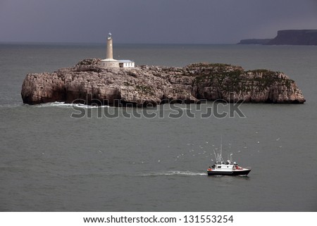 Island lighthouse  / Small fishing boat sailing near Mouro Island lighthouse in stormy weather. North Spain,