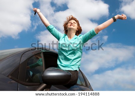 young girl sitting in the car and holding a key against blue sky