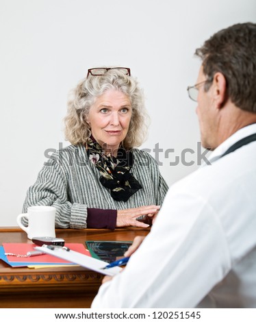Mature woman patient consults with doctor in his office. Focus is on the woman.