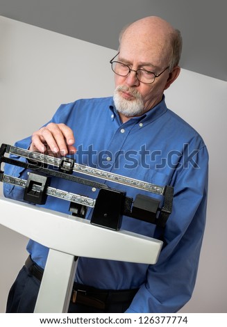 Senior caucasian man weighing himself on vertical weight scale. He looks thoughtful and concerned.