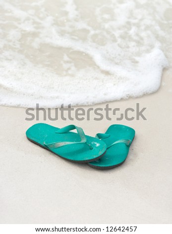 A pair of blue-green flip flops (thong sandals) at the water\'s edge at the beach. Good background shot.
